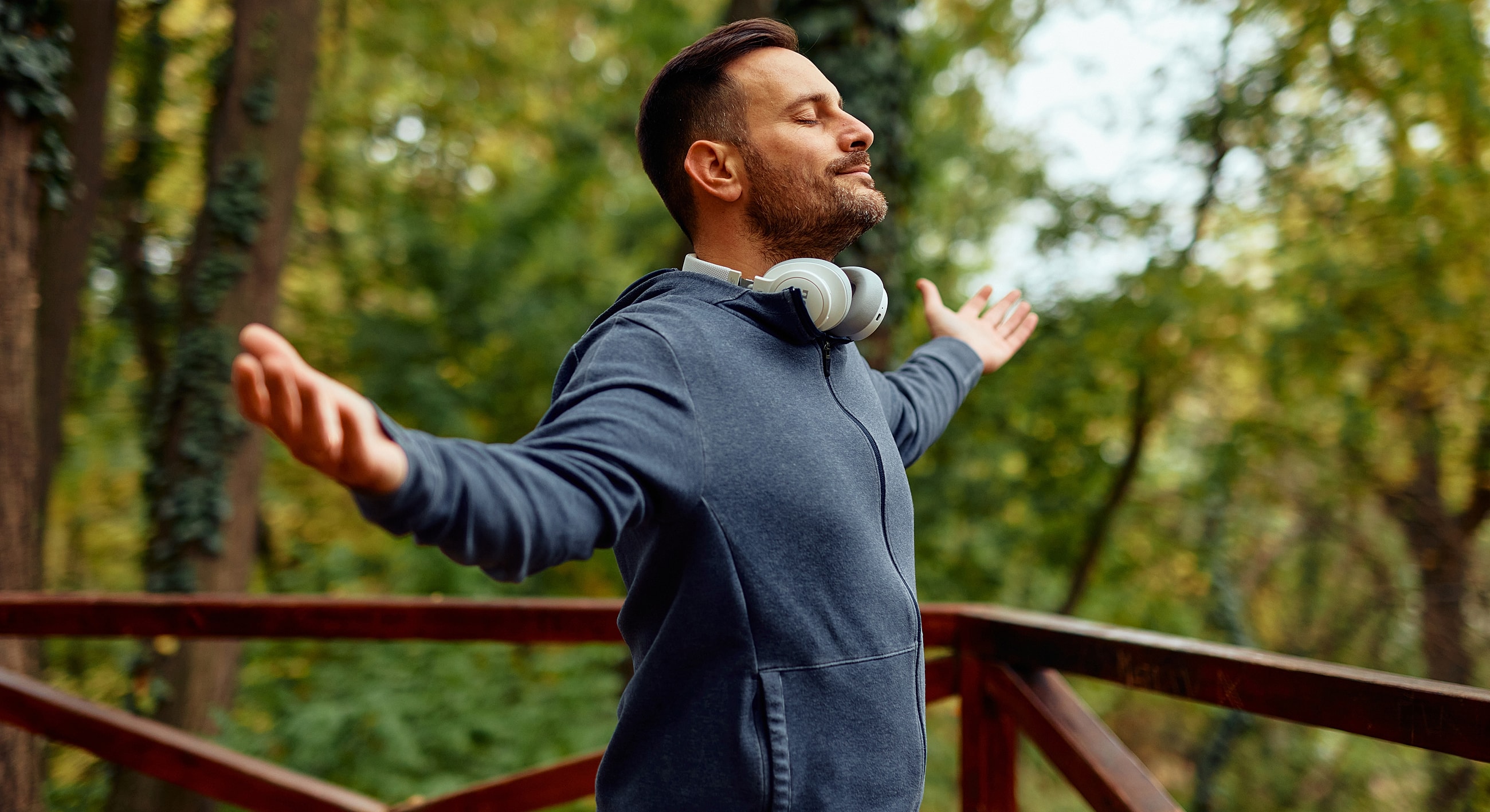 Man enjoying nature with headphones, arms outstretched.